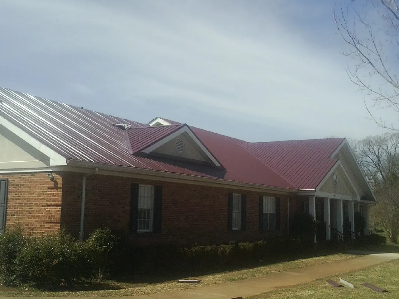 Red metal roof with gabled entries on a long brick building, from a Hail Damage Roof Repair job in Brierfield