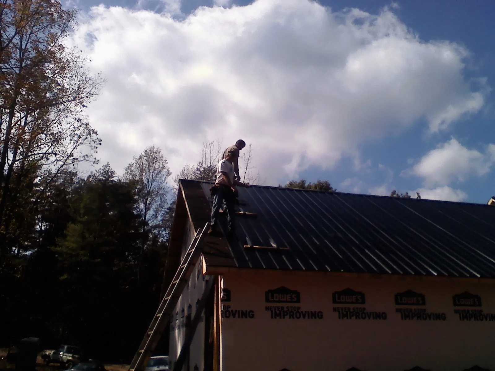 Roofer fastening dark metal panels high against a cloudy sky, from a Roof Inspection job in Brierfield
