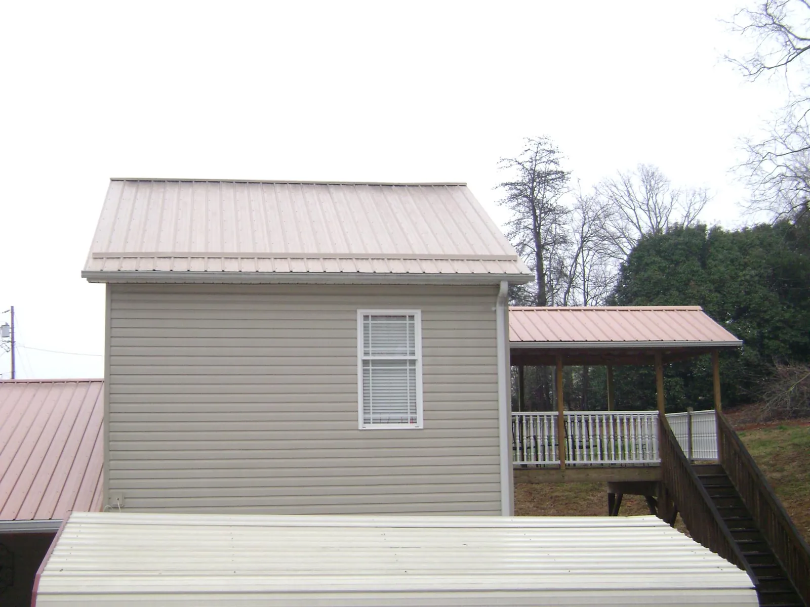 Tan metal roofs on a two story addition and attached porch, from a Roof Replacement job in Brierfield